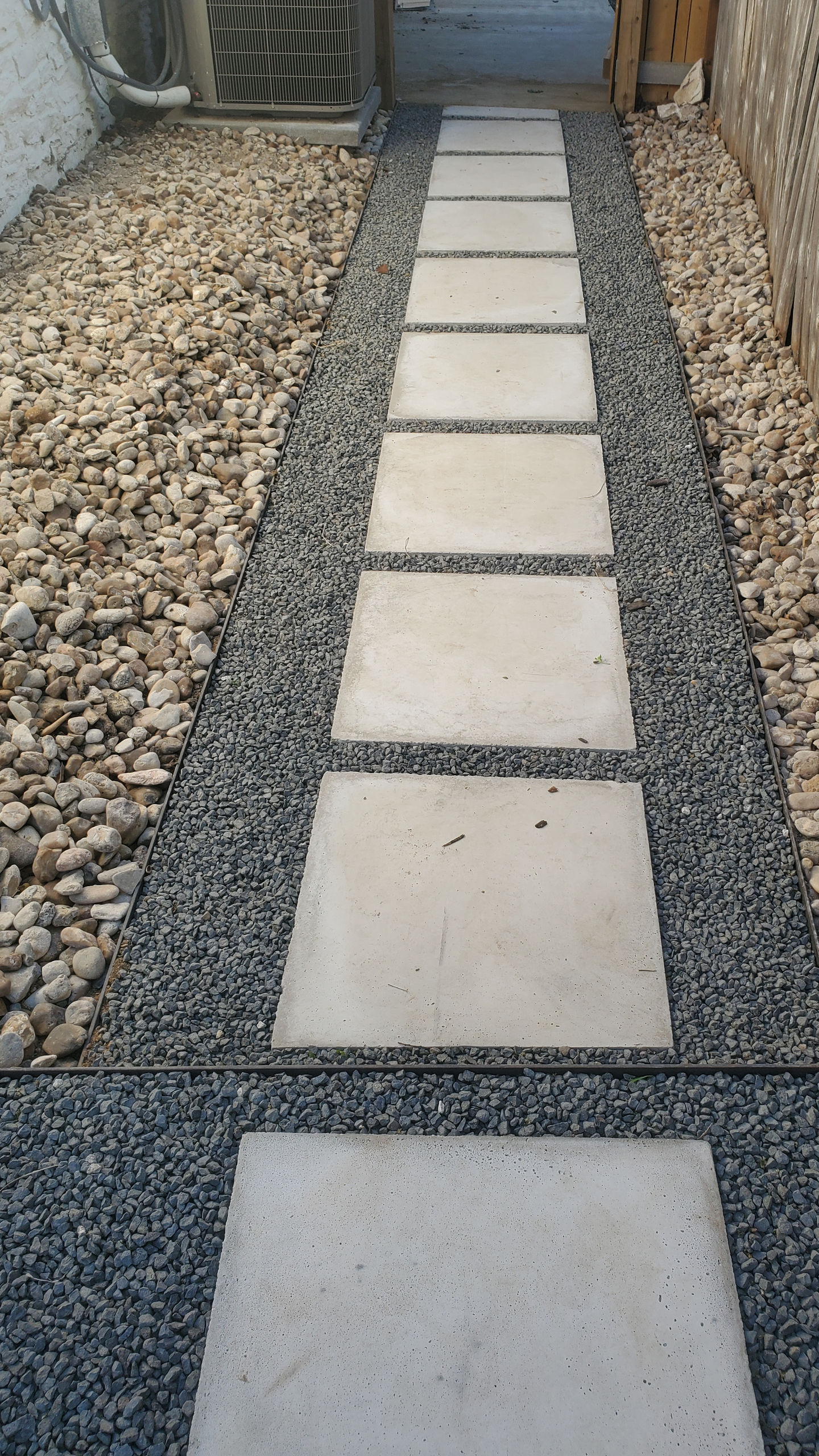 a walkway with concrete slabs and gravel in the background