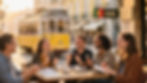 Expats practicing European Portuguese with an instructor at a Lisbon café as a yellow tram passes.