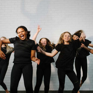 Girls dressed in black dance clothes, dancing and laughing