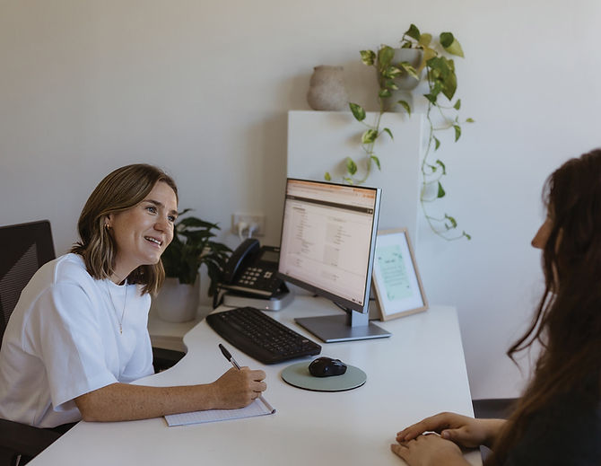 A woman at a computer listening and smiling.
