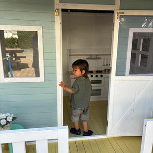 Toddler at the doorway to an aqua and white painted wooden cubby house