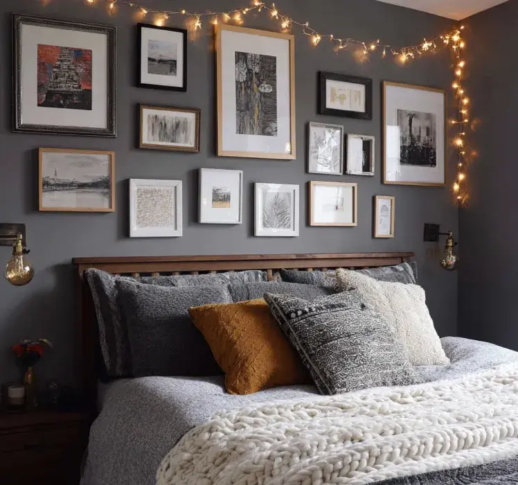Cozy bedroom design with a dark gray accent wall, gallery wall of framed art, warm string lights, layered throw pillows, textured knit blanket, and rustic wooden headboard.