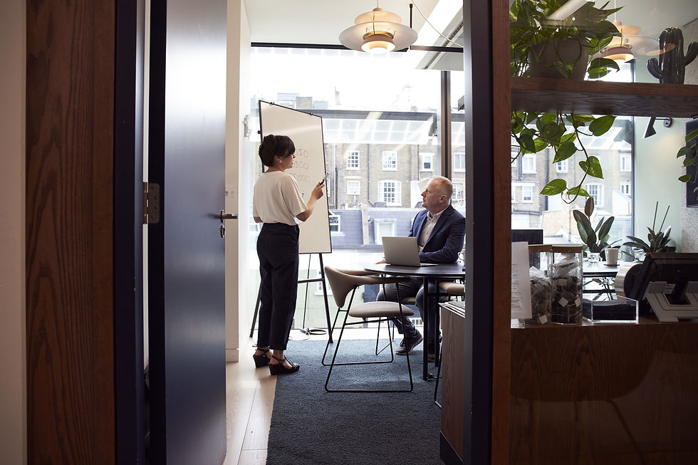 A young nab and woman interact about business in a well lit office with big windows and green plants.