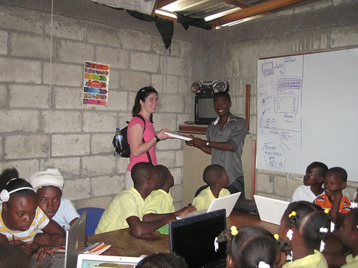Julia Rathmann-Bloch and Wenley Moise pose with a computer in front of a class of students at SAKALA
