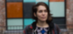 Girl with nose ring wearing a colorful prints standing in front of color blockd windows and a brick wall