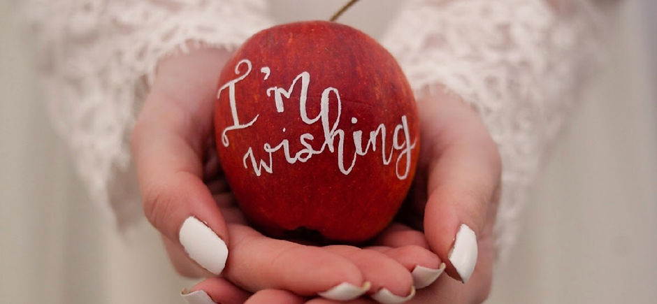 A bride dressed in white, with fingernails painted white, as a 'Snow White' bride. She is holding an apple, hand lettered with the words 'I'm wishing'