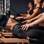 Close up of women doing pilates on reformer wearing black sportswear, on a dark bl