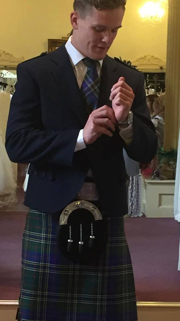 Scottish rugby's Darcy Graham wearing Hawick Tartan kilt, waistcoat, and bowtie with kilt jacket, socks, and sporran. Fixing his cuff.
