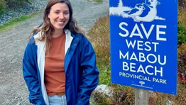 Local resident smiling next to a lawn sign at West Mabou Beach Provincial Park