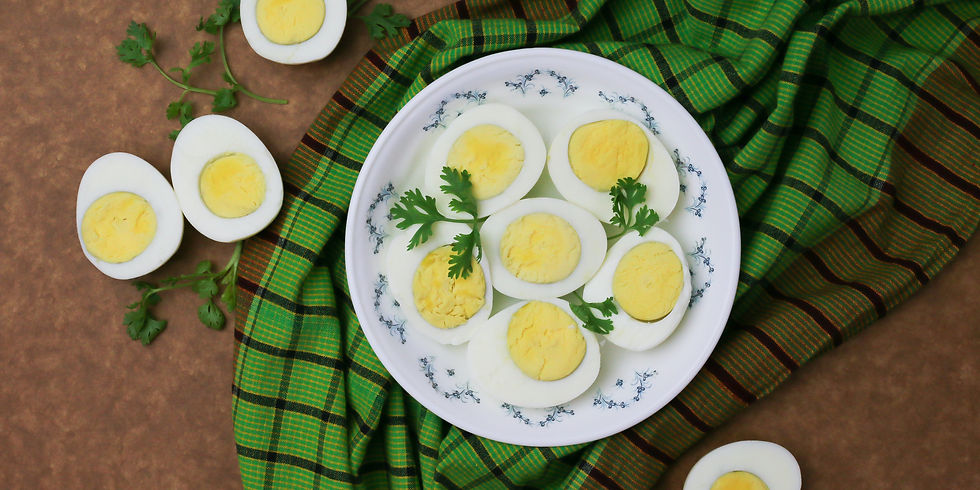 Sliced boiled eggs on a white plate with parsley, set on a green plaid cloth. Brown background with cilantro leaves scattered.
