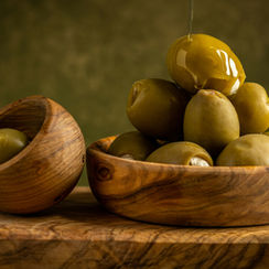 Fresh green olives, gleaming with oil, rest elegantly in a wooden bowl on a matching cutting board, capturing the essence of a Mediterranean delight.