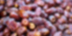 Close-up of glossy, ripe dates in warm brown tones, filling the frame. The texture is wrinkled and richly detailed, evoking a natural, wholesome feel.