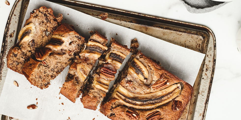 Sliced banana bread on a baking sheet with pecans and banana slices on top. The bread sits on parchment, creating a cozy, homemade feel.