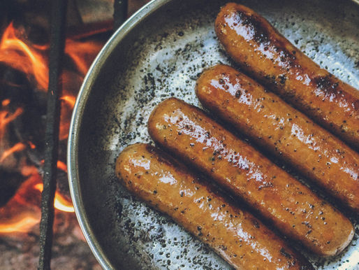 Sausages sizzling in a pan over an open flame, creating a perfect meal on the grill.