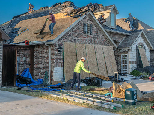 Roofers work diligently on a residential home, carefully laying new shingles while surrounded by ladders and materials on a sunny day.