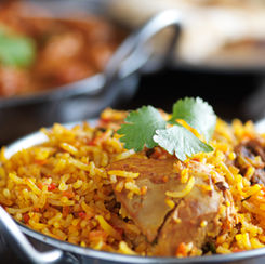 Aromatic chicken biryani garnished with fresh cilantro, served in a traditional metal dish, offering a delicious blend of spices and flavors.