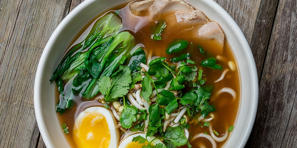 Bowl of ramen on a wooden table with bok choy, boiled egg, sliced meat, green onions, and cilantro in broth, creating a savory mood.