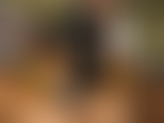 Close-up of three cannabis vape cartridges on a wooden surface, filled with golden oil, with blurred cannabis buds in the background.