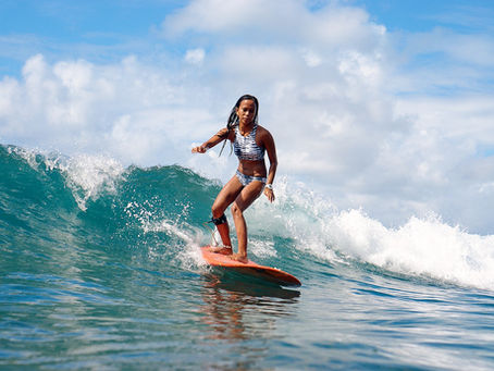 Filipina surfer riding a clean wave on a red longboard in Siargao, Philippines, under a bright blue sky.