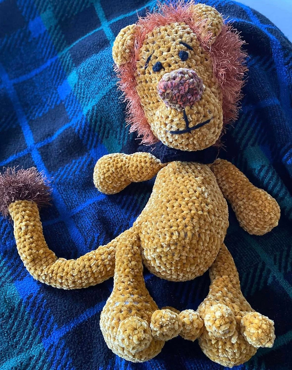 Crocheted lion toy on a blue and green plaid blanket. The lion has a brown mane and a cheerful expression, creating a cozy vibe.