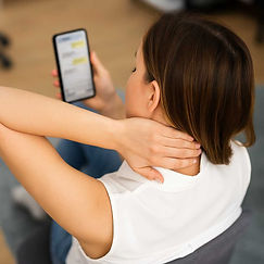 A young woman seated and looking down at her smartphone, holding her neck in discomfort — a realistic image reflecting the impact of tech neck.