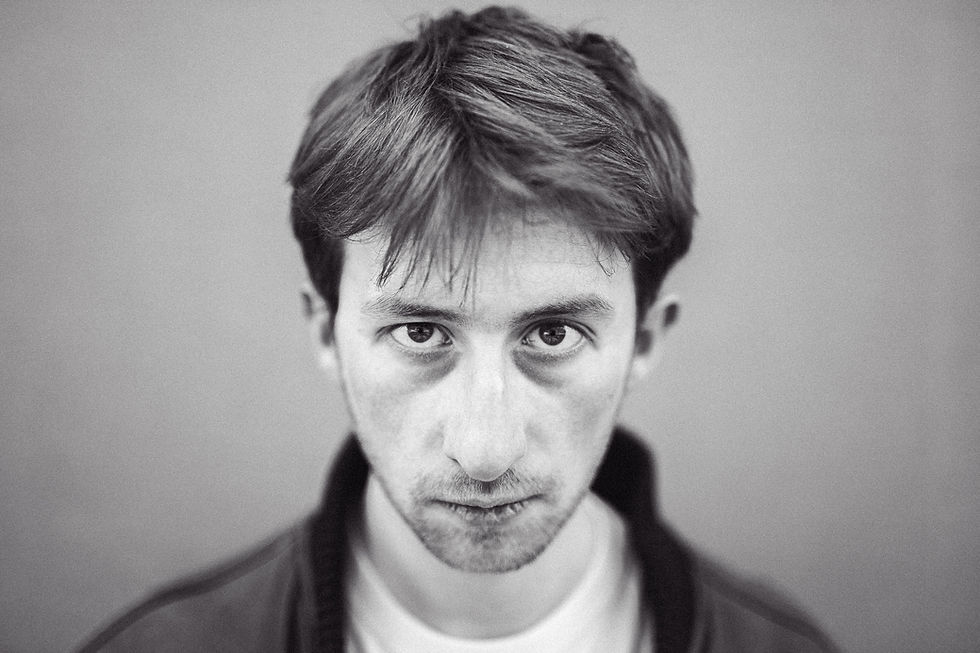 Schauspielportrait mit Anton Giuseppe Arnold: Schwarzweiß-Porträt eines Mannes mit kurzem Haar. Er schaut direkt in die Kamera. Hintergrund unscharf.