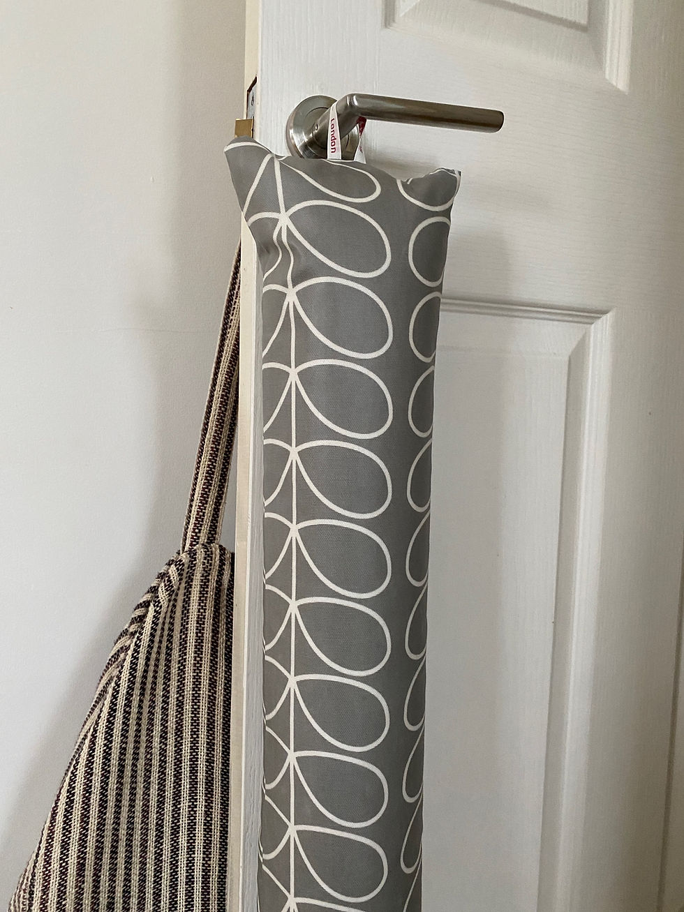 Thumbnail: Light grey draught excluder hanging from door handle.