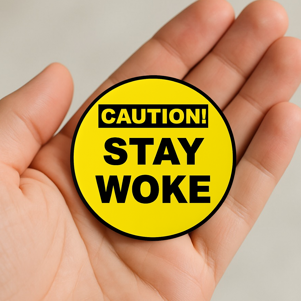 Yellow circular pin badge reading “Caution! Stay Woke” in bold black text, held in a hand