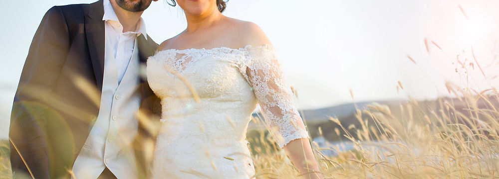 Photograph of a happy wedded couple are holding and standing side to side in a golden field