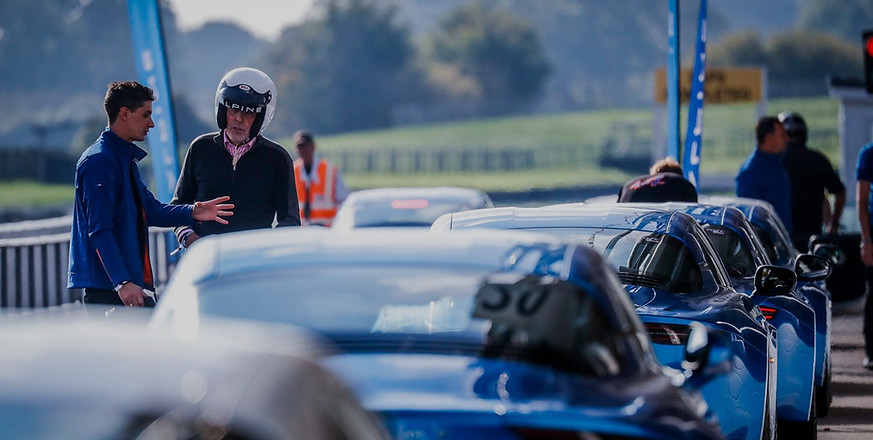Un instructeur discute avec un pilote dans la pitlane ou sont alignées des Alpine A110