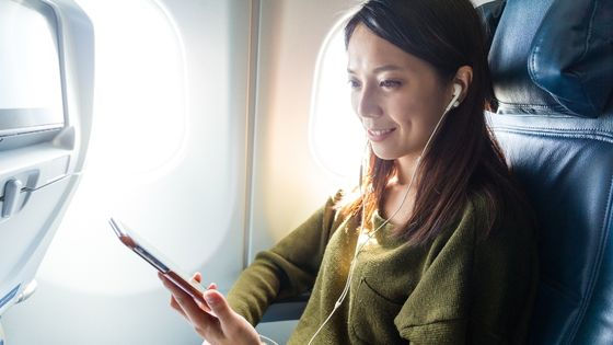 woman with headphones on a plane looking at phone in her hand