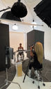 Photographer photographing a seated model in a studio with lighting equipment and reflectors.