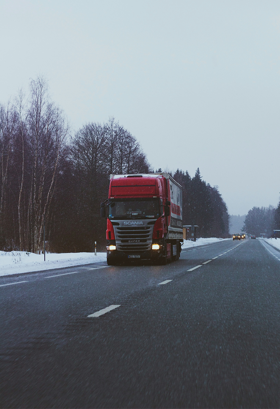 Camion Scania rouge sur une route enneigée.