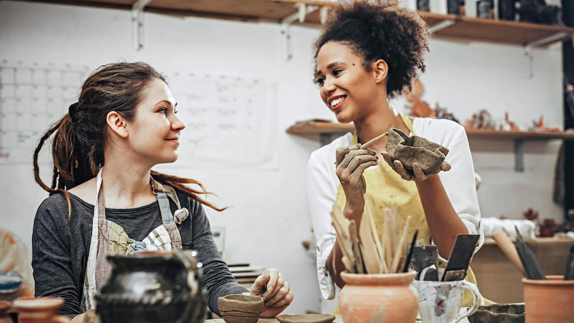 two women doing pottery and smiling together