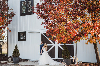 Bride and groom standing in front of a white barn reading vows to one another