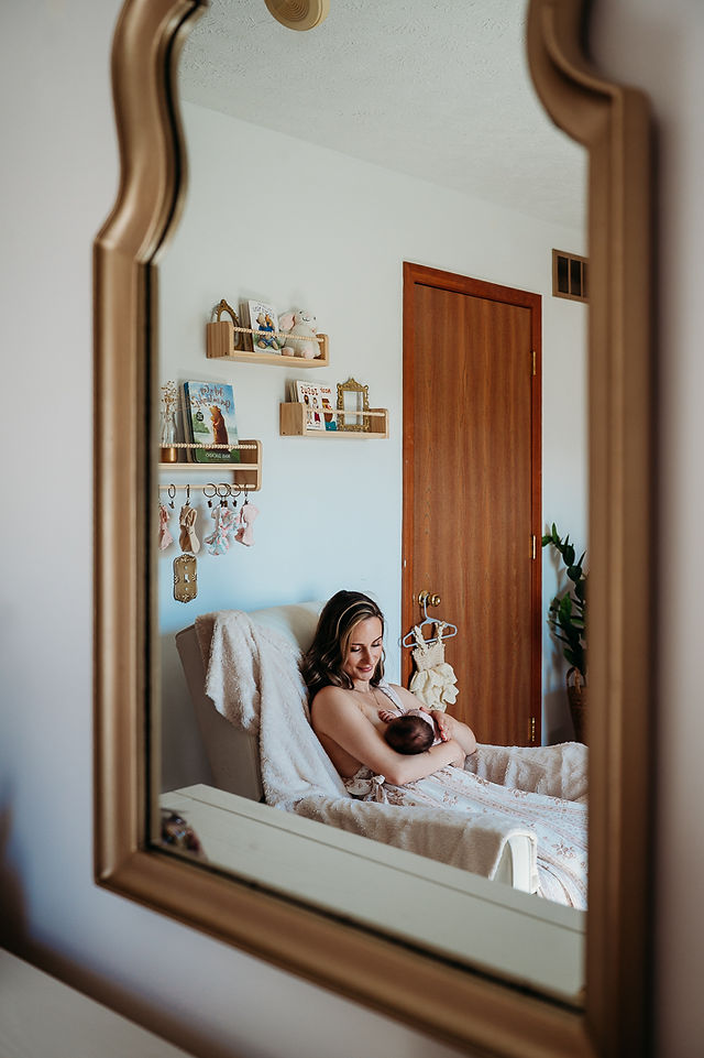 Reflection in a mirror of a mom sitting in the nursery chair holding her newborn baby
