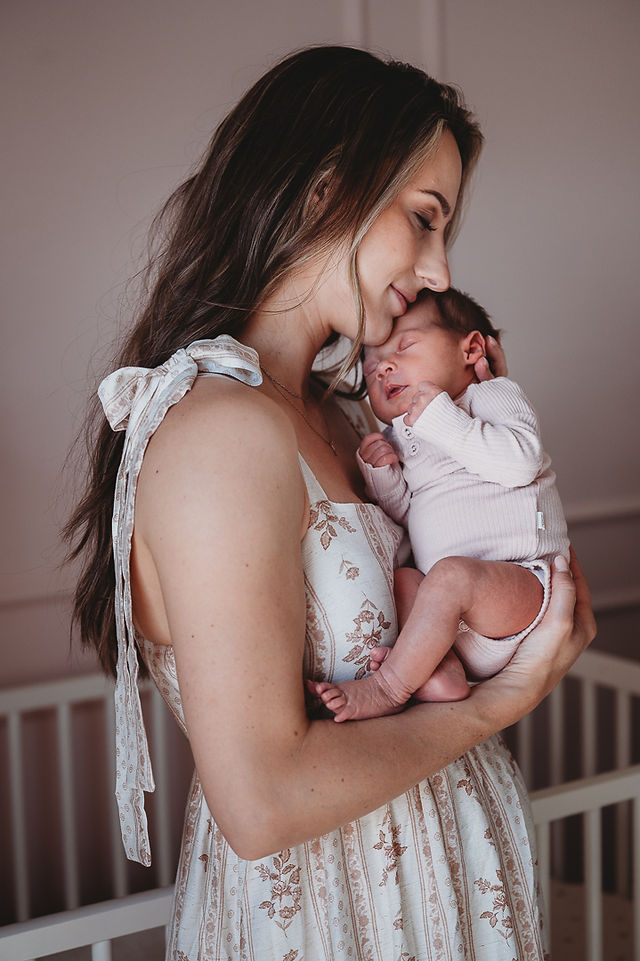 A mom standing in front of a white crib holding her newborn up to her face
