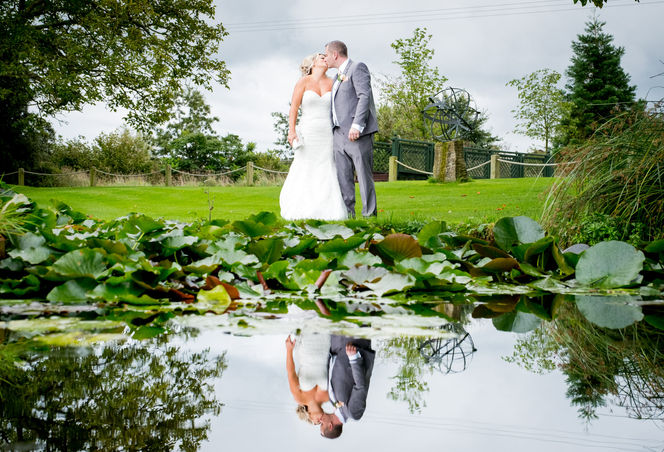 Bride and groom kissing with reflection in the pond at Parley Manor