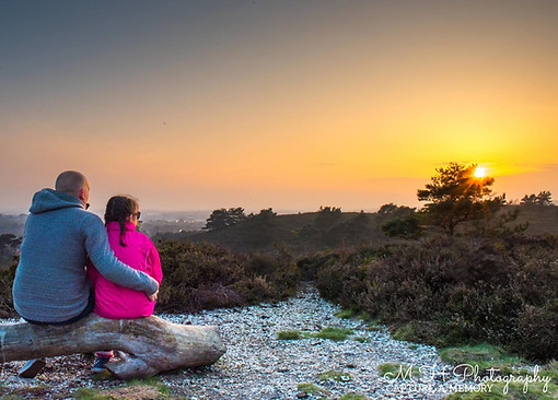 Marcus Horwood sitting with his daughter watching the sunset at Canford Heath in Dorset