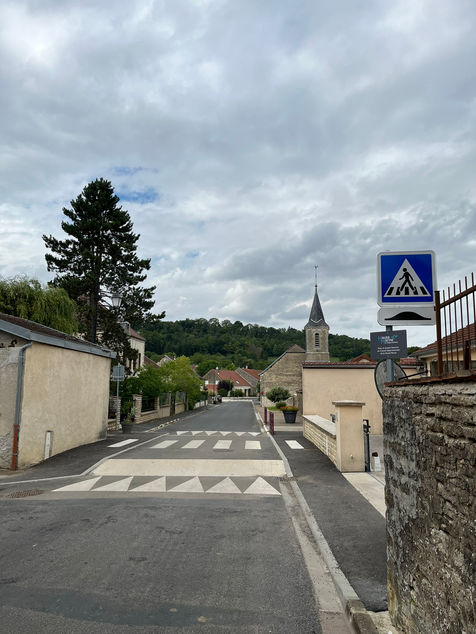 Rue du village de Buxières-lès-Villiers, en Haute-Marne, dans le Grand-Est, en France. Cette rue comporte un nouveau revêtement en enrobé, des ralentisseurs pour sécuriser le village, des nouveaux panneaux de signalisation... La photo montre l'église du village en arrière-plan.
