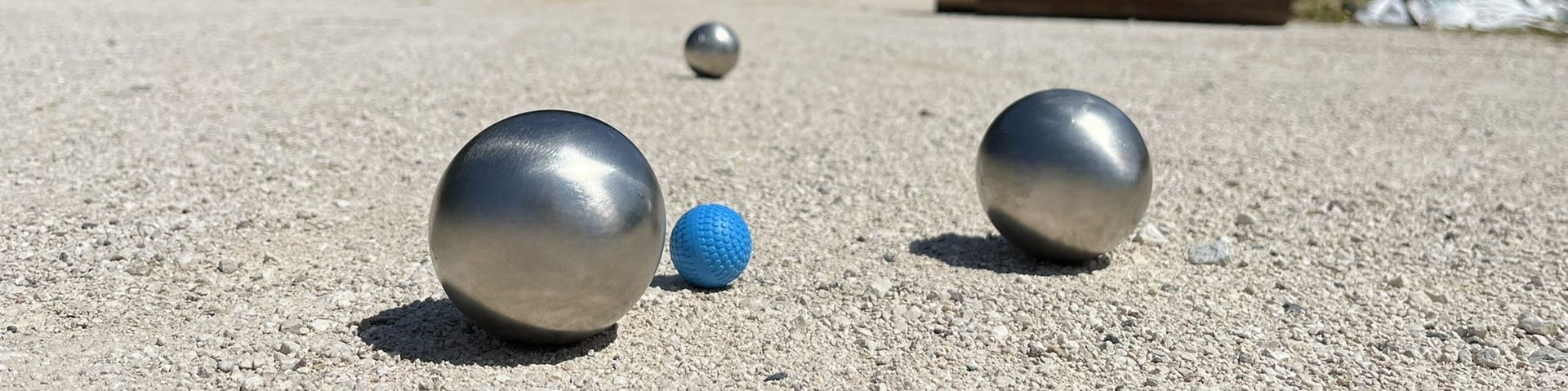 Vue très zoomée de trois boules de pétanque et d'un cochonnet, disposés sur un terrain de pétanque, surfacé avec des gravillons blancs fins