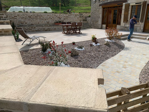 Photo d'une cour d'un particulier avec un muret en pierres, une aire de végétation avec pierres décoratives et gravier, une allée en pierre et une terrasse en dalles. Chantier réalisé par la SAS André BOUREAU dans l'Aube, dans le Grand-Est, en France.