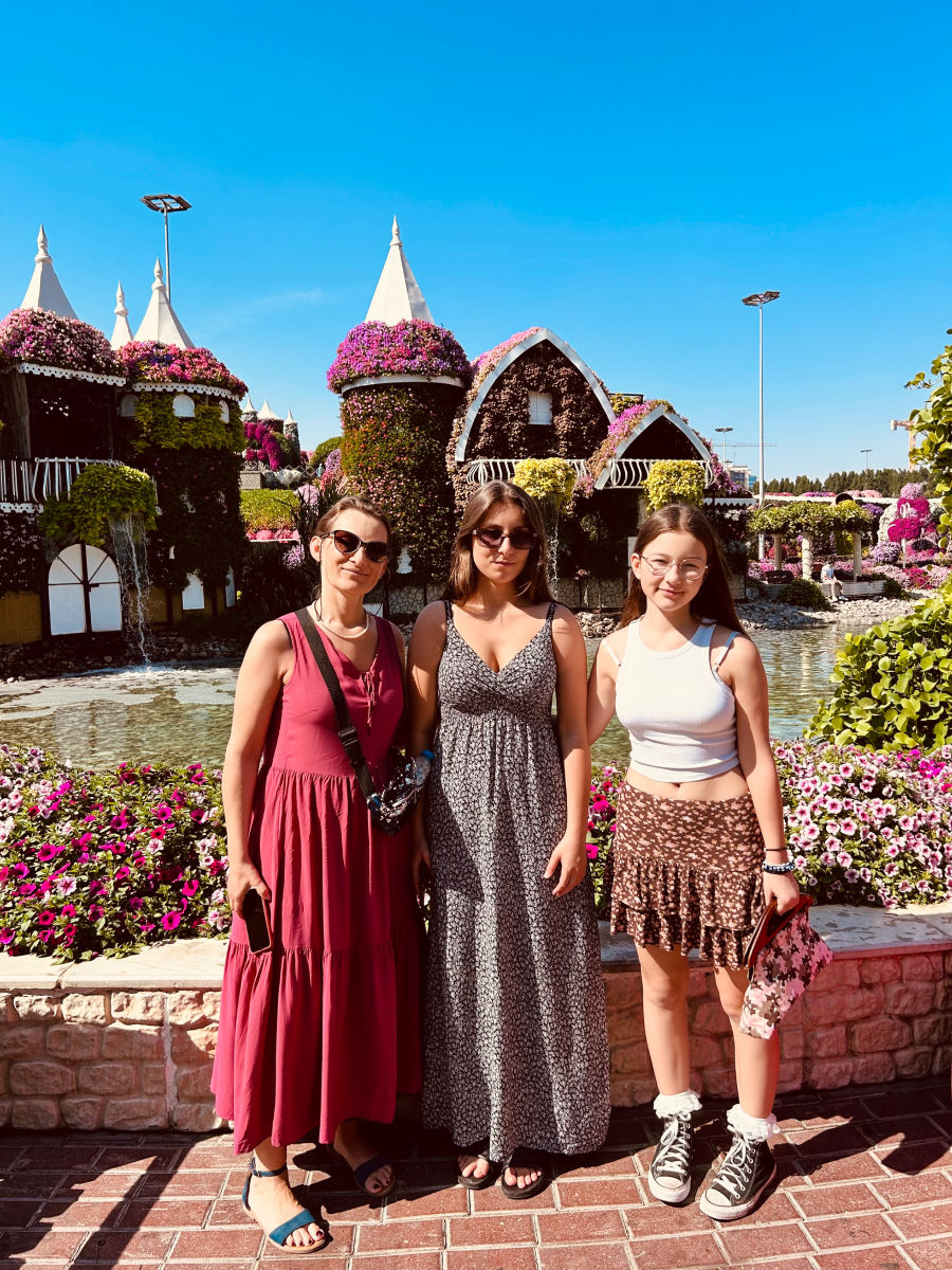 Trzy uśmiechnięte panie pozują do zdjęcia w Miracle Gardens na tle zamku z kwiatów