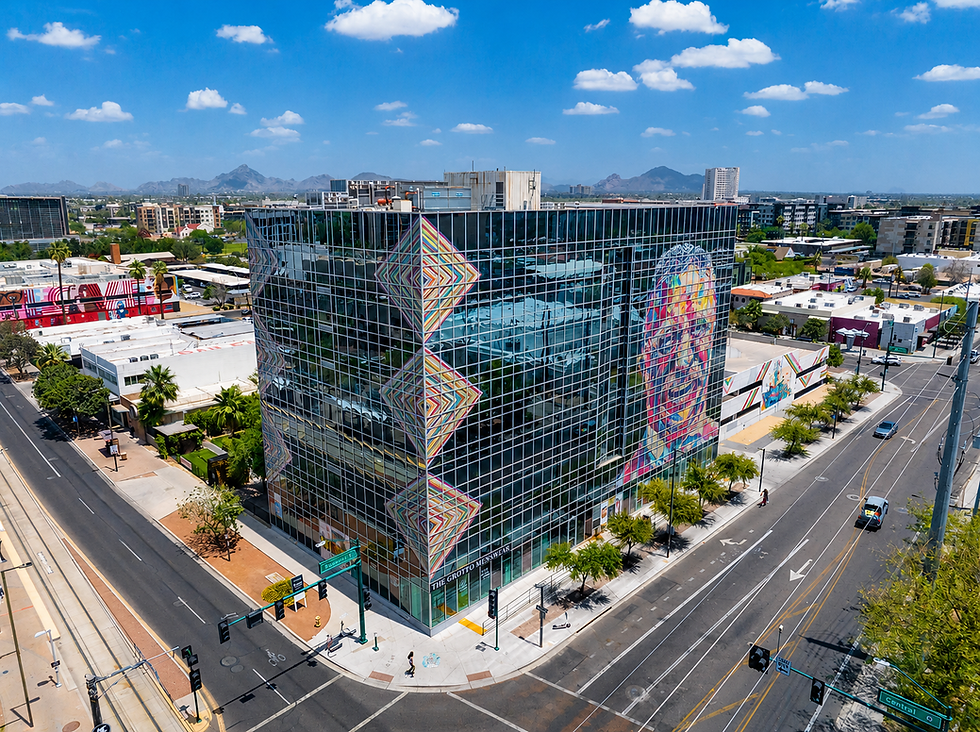External shot of the Heart & Soul Office, a modern glass building with colorful geometric murals and a large vibrant portrait. Blue skies and distant mountains add to the urban landscape.