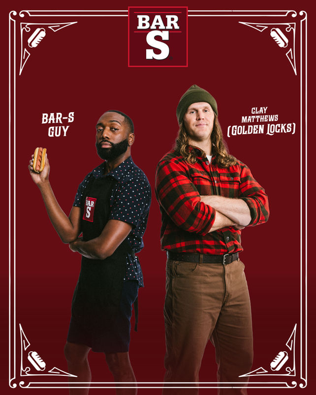 Two men stand back-to-back against a burgundy backdrop. One in an apron holds a hot dog; the other wears a red plaid shirt and a beanie. Text reads, "Bar-S Guy" and "Clay Matthews."