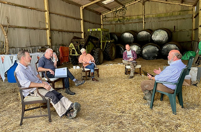 A group of adults sit in a barn, some are looking at manuals and one is teaching the others