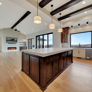 Open kitchen and living space by Murray Custom Homes designed with wood island, vaulted ceiling, and large windows.