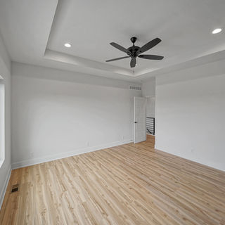 Murray Custom Homes designed empty bedroom with wood floors, tray ceiling, ceiling fan, and large window.