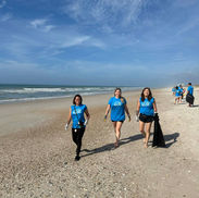 Three women in blue shirts cleaning a sandy beach