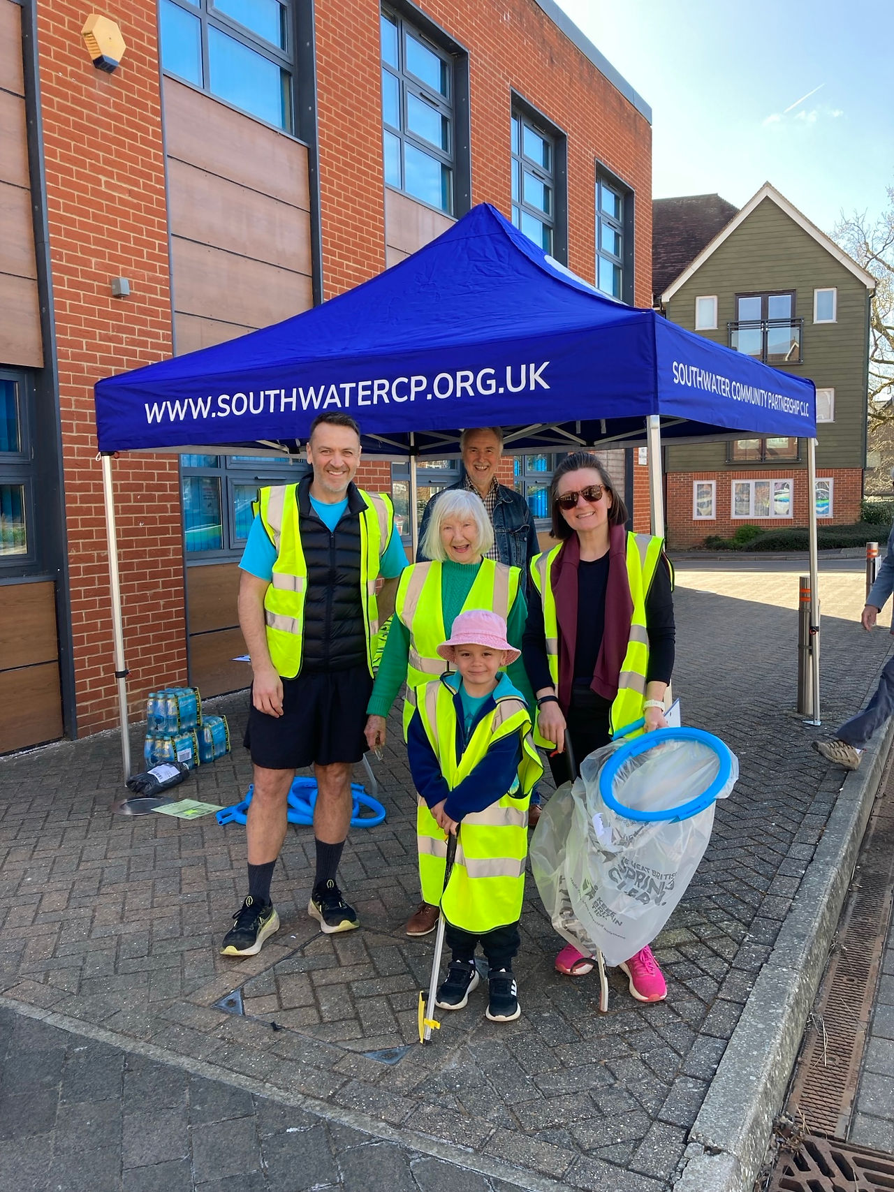 A family of 5 people in high visibility vests and litter picking equipment. 